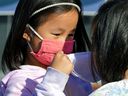 Tessa Ng, age 5, helps a friend put on a face mask in a file photo from Edmonton from Nov. 19, 2021. Certain media have been scaremongering regarding the risks posed by the coronavirus to children, say three experts.