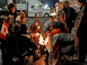 Die Menschen wärmen sich am 15. Februar 2022 in Ottawa an einem Feuer auf dem Parliament Hill auf, während Trucker und Unterstützer weiterhin gegen die COVID-19-Beschränkungen protestieren.