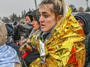 Eine Ukrainerin drückt ihren kleinen Hund fest an ihre Brust, während sie in der Schlange im Aufnahmezentrum in Medyka an der polnisch-ukrainischen Grenze wartet.  Eine Rettungsdecke ist um ihre Schultern gewickelt, um ihr zu helfen, sich vor der bitteren Winterkälte warm zu halten.  (Foto: Milos Bicanski/We Animals Media)