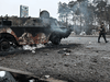 An armed man walks past a burned armoured personnel carrier (APC) BTR-4 on a check-point in the city of Brovary outside Kyiv on March 1, 2022.