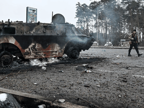 Ein bewaffneter Mann geht am 1. März 2022 an einem Kontrollpunkt in der Stadt Browary außerhalb von Kiew an einem verbrannten Schützenpanzer (APC) BTR-4 vorbei.