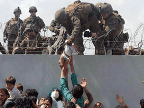 A U.S. Marine hoists an infant over a fence of barbed wire during an evacuation in Kabul last August. Many Afghans remain stuck in bureaucratic limbo as they wait to immigrate.