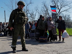 A service member of a pro-Russian troop stands guard as evacuees wait to board a bus to leave the city of Mariupol, Ukraine, on April 20, 2022.