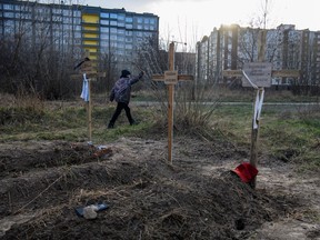 A boy walks past graves with bodies of civilians, who according to local residents were killed by Russian soldiers, as Russia's attack on Ukraine continues, in Bucha, in Kyiv region, Ukraine April 4, 2022. The inscription on the cross in the middle reads: "Unknown". REUTERS/Vladyslav Musiienko