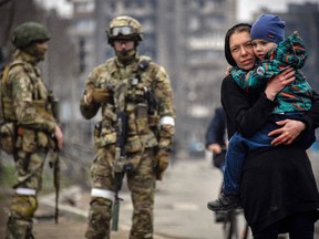 Eine Frau hält am 12. April ein Kind neben russischen Soldaten in einer Straße von Mariupol.