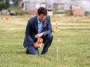 Prime Minister Justin Trudeau lays a teddy bear on a small flag in a field before a ceremony at the site of a former residential school in Cowessess First Nation, Saskatchewan, July 6, 2021.