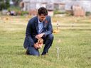 Prime Minister Justin Trudeau places a teddy bear on a small flag in a field before a ceremony at the site of a former residential school on July 6, 2021, on Cosseth First Nation in Saskatchewan.