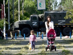 This photo taken on May 20, 2022 shows a womand and child walking in a park as Russian servicemen patrol the street in Skadovsk, Kherson Oblast, amid the ongoing Russian military action in Ukraine.