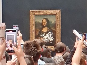 A man tries to wipe off the cake smeared on the protective glass of the painting "Mona Lisa" at the Lourve Museum in Paris, France May 29, 2022 in this screen grab obtained from social media video. Twitter/@klevisl007