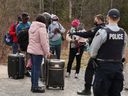 Asylsuchende sprechen mit einem Polizisten, als sie am 24. April 2022 von der US-Grenze in der Nähe eines Kontrollpunkts an der Roxham Road in der Nähe von Hemmingford, Quebec, Kanada, nach Kanada einreisen. 
