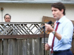 Ein Mann sieht zu, wie Kanadas Premierminister Justin Trudeau am 24. Mai 2022 in Vancouver, British Columbia, Kanada, mit Reportern vor einem Haus spricht, wo er sich mit Bewohnern traf, um über Investitionen des Bundes in den Wohnungsbau zu diskutieren. FOTO VON