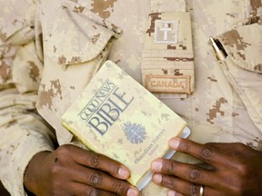 A military chaplain holds a copy of a camouflage bible designed for the Canadian Forces.