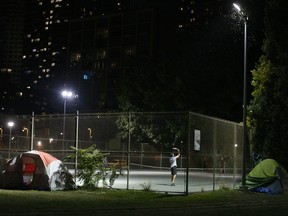 People play tennis next to an homeless encampment in Toronto,, Sept. 23, 2020.