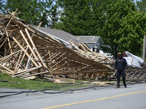 A person walks past a part of the roof of a hardware store that lifted off and crashed into neighbouring houses during a major storm, in the community of Hammond in Clarence-Rockland, Ont., on Monday, May 23, 2022.