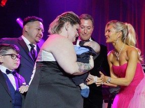 Guests of Honour Jonathon and Christine Fischer, right, meet the new baby carried by surrogate Samantha Audia for the Chen family, left, onstage at a fundraiser for the David Foster Foundation in Toronto, Ont., May 7, 2022.