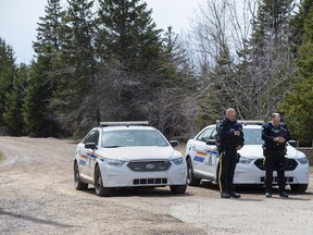 Two RCMP officers observe a moment of silence to honour slain Const. Heidi Stevenson and the other 21 victims of the mass killings at a checkpoint on Portapique Road in Portapique, N.S. on Friday, April 24, 2020.