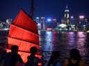 Tourist take pictures in front of a traditional Chinese junk boat as the Hong Kong skyline is seen across Victoria Harbour. 