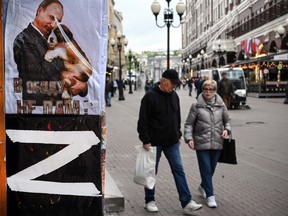 People walk past a gift shop in Moscow on May 17, 2022, next to t-shirts showing Vladimir Putin or bearing the letter Z, which has become a symbol of support for Russian military action in Ukraine. Polls suggest that more than half of Russia's population supports Putin's invasion of Ukraine.