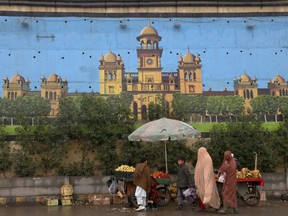 A family walk past a huge mural of historical Islamia College building painted on an overhead bridge wall, in Peshawar, Pakistan, Friday, Jan. 7, 2022. An international watchdog said Friday, June 17, it will keep Pakistan on a so-called "gray list" of countries that do not take full measures to combat money-laundering and terror financing but raised hopes that its removal would follow an upcoming visit to the country to determine its progress.