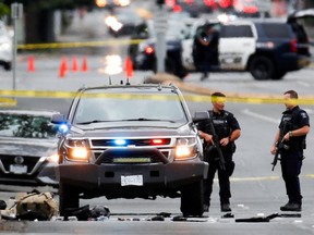 Police officers gather after two armed men entering a bank were killed in a shootout with police in Saanich, B.C., June 28, 2022.