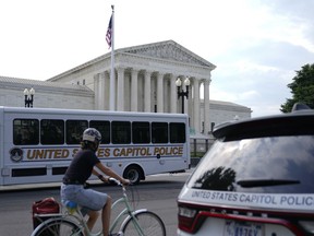 A bicyclist rides past police vehicles parked outside the U.S. Supreme Court building, Monday, June 27, 2022, in Washington.
