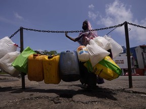 A woman stands by empty vessels that are seen tied up in a line to secure positions of a queue for buying kerosine oil outside a fuel station in Colombo, Sri Lanka, Sunday, June 5, 2022. The country is facing its worst economic crisis in recent memory.