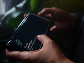 Eine Person hält in einer Fotoillustration ein Smartphone an den Startbildschirm der ArriveCan-App.
