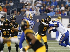 Hamilton Tiger-Cats quarterback Dane Evans (9) gets the throw away despite pressure from Winnipeg Blue Bombers' Willie Jefferson (5) and Jackson Jeffcoat (94) during the first half of CFL action in Winnipeg, Friday, June 24, 2022.