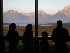 FILE - Visitors watch the morning sun illuminate the Grand Tetons from within the Great Room at the Jackson Lake Lodge in Grand Teton National Park in Wyoming on Aug. 28, 2016. Heather Mycoskie, 40, accused of intentionally providing wrong information in the search for a missing man in Grand Teton National Park has been banned from the park and ordered to pay restitution.