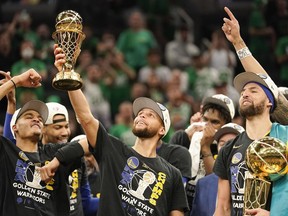 Golden State Warriors guard Stephen Curry, center, holds up the Bill Russell Trophy for most valuable player after the Warriors defeated the Boston Celtics in Game 6 to win basketball's NBA Finals championship, Thursday, June 16, 2022, in Boston.