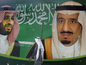 In this March 7, 2020 file photo, a man walks past a banner showing Saudi King Salman, right, and his Crown Prince Mohammed bin Salman, outside a mall in Jiddah, Saudi Arabia.