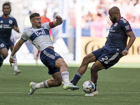 Vancouver Whitecaps' Lucas Cavallini, left, tries to push the the ball past New England Revolution's Andrew Farrell during first half MLS soccer action in Vancouver, B.C., Sunday, June 26, 2022.