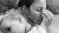 A sad mother covering her face depressed and unhappy holding her child in black and white.