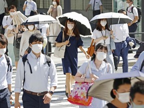 People, some of them holding parasols, cross an intersection amid heat, in Tokyo, Monday, June 27, 2022. Japan's government issued a warning for possible power crunch in the Tokyo area Monday, asking offices and residents to save energy as the capital region is hit by sweltering heat, with weather officials announcing an earliest end to the rainy season in decades.