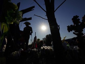 Roberto Marquez adds a cross to a makeshift memorial at the site where officials more than 50 people dead in an abandoned semitrailer containing suspected migrants, Thursday, June 30, 2022, in San Antonio.