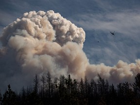 A helicopter carrying a water bucket flies past a pyrocumulus cloud, also known as a fire cloud, produced by the Lytton Creek wildfire burning in the mountains above Lytton, B.C., on Sunday, August 15, 2021. The Insurance Bureau of Canada says there is now a path to begin the recovery of the Village of Lytton, almost a year after two people died and most of the community was destroyed by a wildfire.