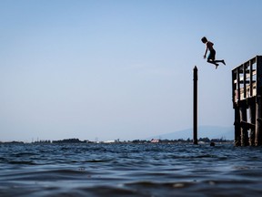 A young boy is silhouetted as he jumps off the pier at Crescent Beach into Boundary Bay, in Surrey, B.C., Tuesday, July 6, 2021.