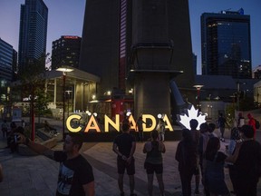 Besucher versammeln sich in der Nähe eines beleuchteten Kanada-Schildes vor dem CN Tower in Toronto.