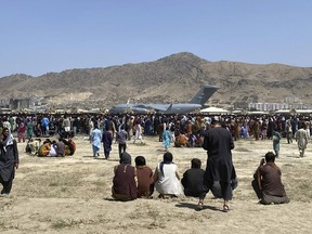 FILE - Hundreds of people gather near a U.S. Air Force C-17 transport plane at the perimeter of the international airport in Kabul, Afghanistan, on Aug. 16, 2021. The independent watchdog for U.S. assistance to Afghanistan is accusing the State Department and U.S. Agency for International Development of illegally withholding information from it about the American withdrawal from the country last year.