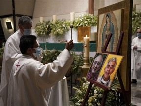 A priest blesses the photos of Jesuit priests Javier Campos Morales, left, and Joaquin Cesar Mora Salazar during a Mass to mourn them, at a church in Mexico City, Tuesday, June 21, 2022. The two elderly priests were killed inside a church where a man pursued by gunmen apparently sought refuge in a remote mountainous area of northern Mexico, the religious order's Mexican branch announced Tuesday.