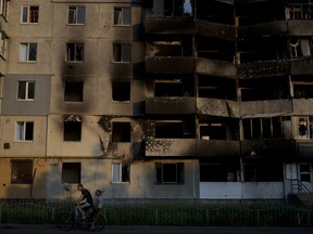 A man rides a bicycle in front of a building destroyed by attacks in Borodyanka, on the outskirts of Kyiv, Ukraine, Sunday, June 12, 2022.