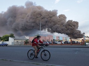 A woman riding a bicycle drives past a cloud of smoke from a fire in the background after a missile strike on a warehouse of an industrial and trading company in Odessa on July 16, 2022, amid the Russian invasion of Ukraine.