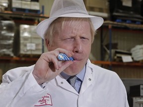 Britain's Prime Minister Boris Johnson eats a candy stick which reads "Back Boris" during a General Election campaign trail stop at Coronation Candy in Blackpool, England, Friday, Nov. 15, 2019.