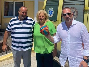 Ivan's father (R) holding the ball that rescued his son, with Mayor Anastasia Halkia (C).