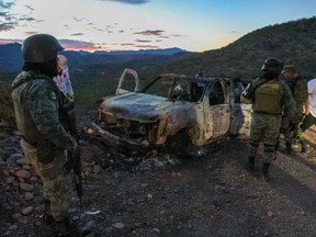 People stand near the burned car where part of the nine murdered members of the family were killed and burned during an ambush in Bavispe, Sonora mountains, Mexico, on Nov. 5, 2019.