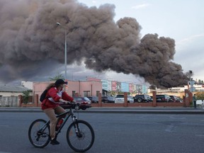 A woman riding a bicycle drives past a cloud of smoke from a fire in the background after a missile strike on a warehouse of an industrial and trading company in Odessa on July 16.