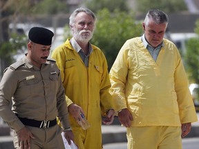 FILE - Volker Waldmann, right, and Jim Fitton, center, are handcuffed as they walk to a courtroom escorted by police arriving to court in Baghdad, Iraq, on May 22, 2022. A retired British geologist jailed in Iraq for antiquities smuggling has been freed and has left the country, his family said Sunday, July 31, 2022. Jim Fitton, 66, was sentenced last month to 15 years in an Iraqi prison. A Baghdad appeals court overturned the conviction and last week ordered his release.