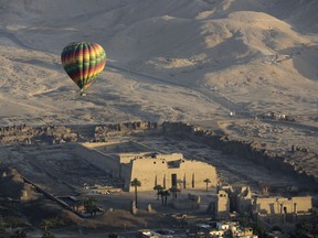 FILE -- A hot air balloon flies over the mortuary temple of Ramsis III at Medinet Habu on the west bank of the Nile River in Luxor, Egypt, April 1, 201. Egyptian authorities suspended hot air ballooning over the ancient city of Luxor after two tourists were lightly injured during a ride early on Monday, July 18, 2022.