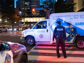An ambulance moves past a member of the Toronto Police in downtown Toronto on Saturday July 16, 2022. Toronto police have provided an update for a homicide investigation into a Saturday evening shooting near Union Station that left one man dead and briefly paused all train and bus services through the busy transportation hub.