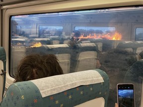 Passengers take photos at a wildfire while traveling on a train in Zamora, Spain, Monday, July 18, 2022. When Francisco Seoane's train unexpectedly stopped in Spanish countryside that was being engulfed by a wildfire, he and other passengers got a fright when they looked out at flames encroaching on both sides of the track. The Spaniard told The Associated Press it was scary to see how quickly the fire spread. Video of the unscheduled -- and unnerving -- stop shows about a dozen passengers in Seoane's railcar appearing alarmed as they look out of the windows Monday.